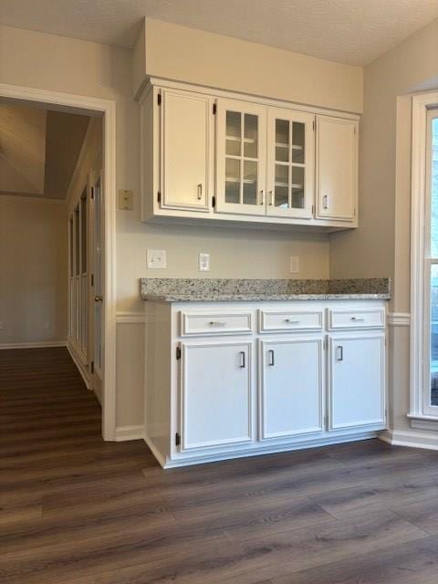 kitchen with dark wood-style floors, white cabinetry, glass insert cabinets, and light stone counters