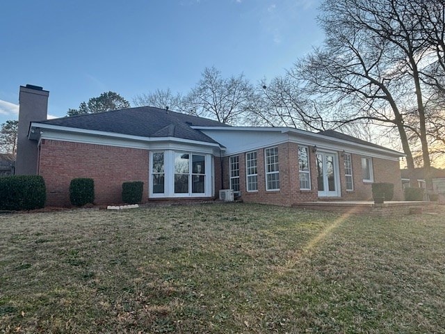 rear view of property featuring a yard, a chimney, and brick siding