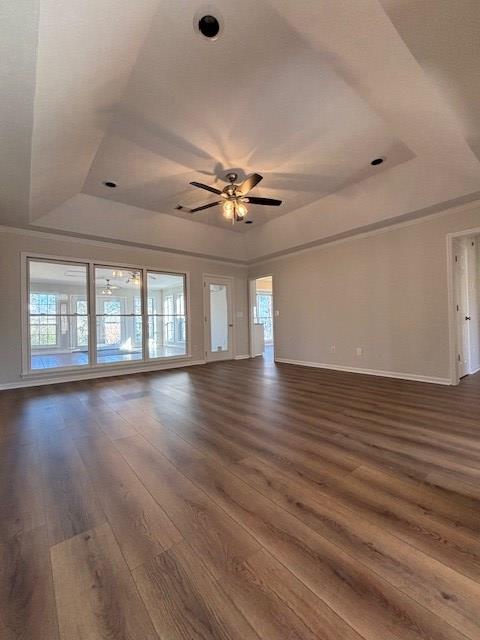 unfurnished living room with baseboards, a tray ceiling, ceiling fan, and dark wood-style flooring