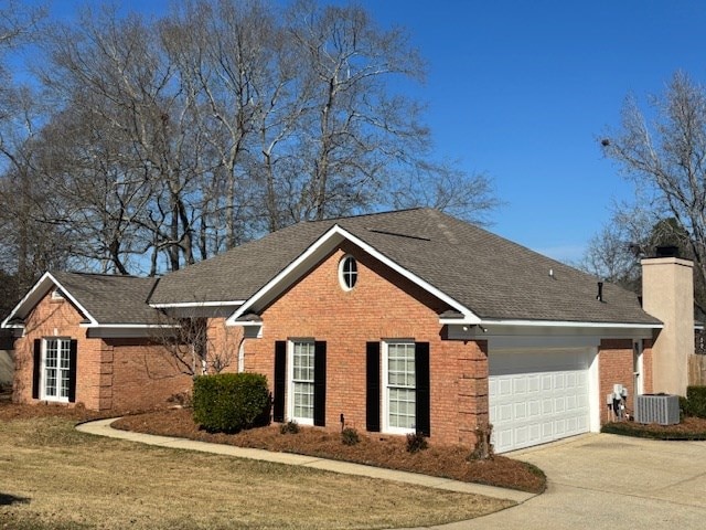 ranch-style home featuring an attached garage, central AC, brick siding, driveway, and a chimney