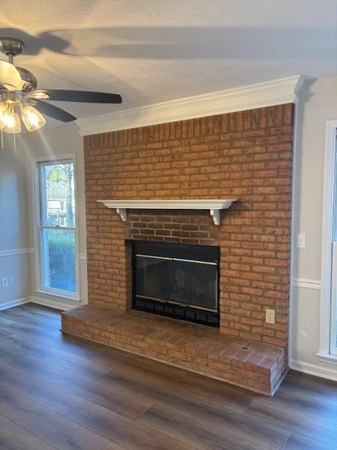 interior details featuring ceiling fan, wood finished floors, baseboards, a brick fireplace, and crown molding