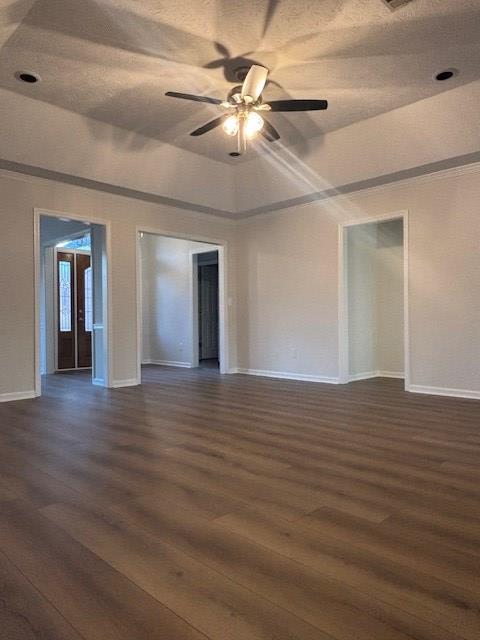 spare room with a ceiling fan, a raised ceiling, dark wood finished floors, and baseboards