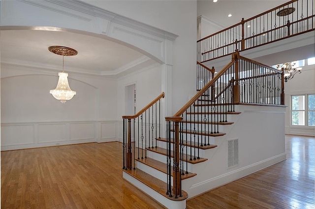 staircase featuring crown molding, wood-type flooring, and an inviting chandelier