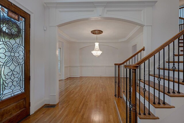 entrance foyer featuring plenty of natural light, an inviting chandelier, ornamental molding, and light wood-type flooring