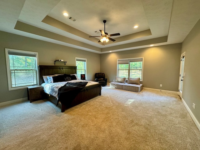 bedroom with a tray ceiling, multiple windows, ceiling fan, and light carpet