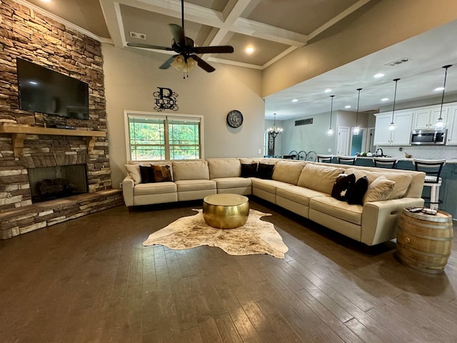 living room featuring dark hardwood / wood-style floors, beam ceiling, a stone fireplace, and ceiling fan with notable chandelier