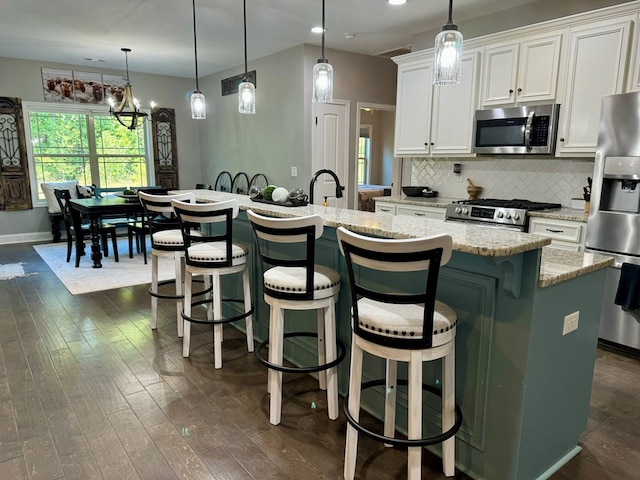 kitchen featuring appliances with stainless steel finishes, dark hardwood / wood-style flooring, pendant lighting, a center island with sink, and white cabinetry