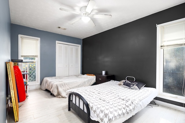 bedroom featuring light hardwood / wood-style flooring, a textured ceiling, ceiling fan, and a closet