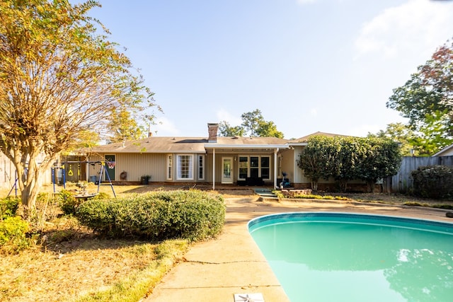 rear view of house with a fenced in pool and a playground