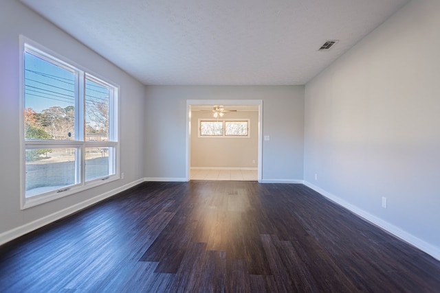 empty room featuring ceiling fan, plenty of natural light, dark wood-type flooring, and a textured ceiling