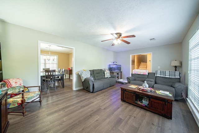 living room featuring a textured ceiling, visible vents, wood finished floors, and ceiling fan with notable chandelier