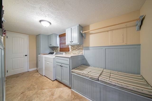 washroom with a textured ceiling, cabinet space, washing machine and clothes dryer, and wainscoting