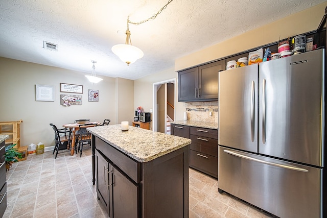 kitchen with a center island, dark brown cabinetry, decorative light fixtures, a textured ceiling, and freestanding refrigerator