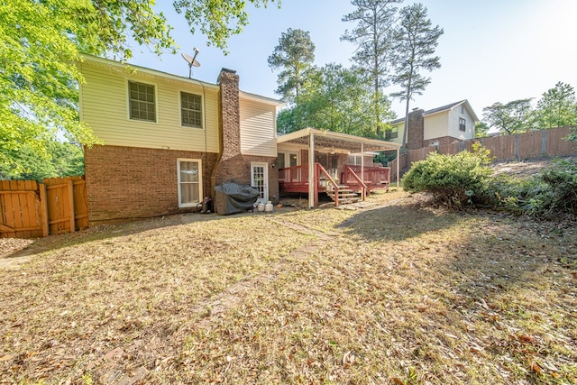 rear view of house featuring a chimney, a deck, a yard, brick siding, and a fenced backyard
