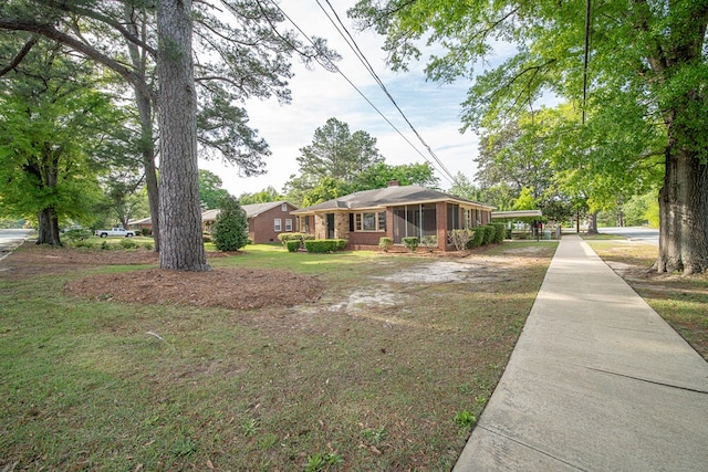 exterior space with a front yard, brick siding, a chimney, driveway, and an attached carport