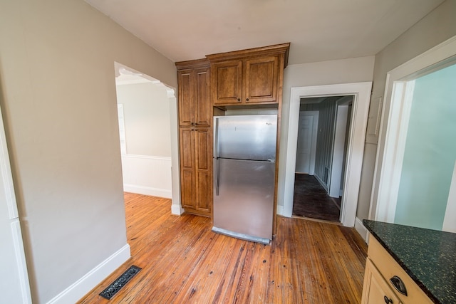 kitchen featuring stainless steel fridge, light hardwood / wood-style floors, and dark stone countertops