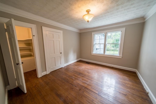 unfurnished bedroom with crown molding, a walk in closet, dark hardwood / wood-style flooring, and a textured ceiling