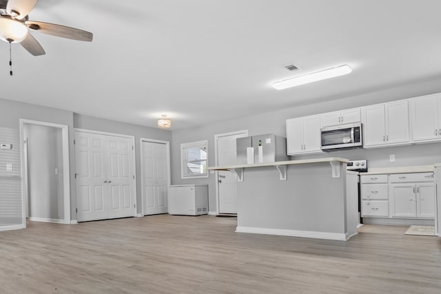 kitchen with a breakfast bar area, light hardwood / wood-style flooring, ceiling fan, white cabinetry, and stainless steel appliances