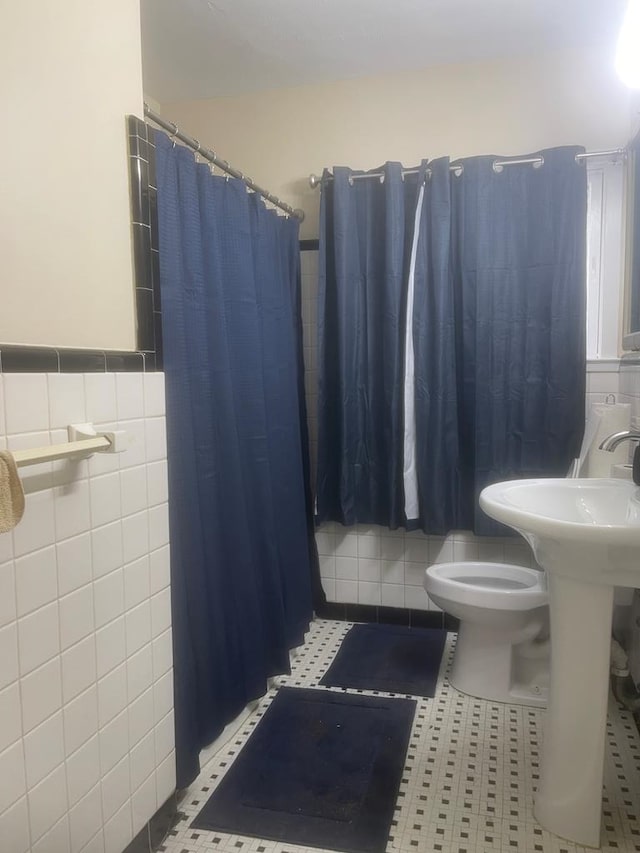 bathroom with toilet, tile patterned floors, tile walls, and curtained shower