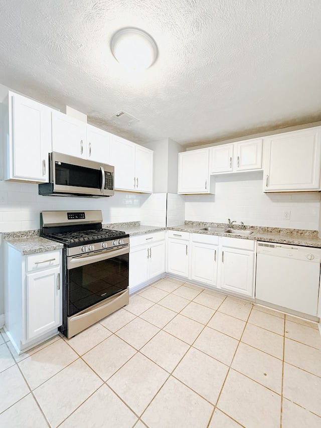 kitchen with a sink, appliances with stainless steel finishes, light tile patterned floors, and white cabinetry