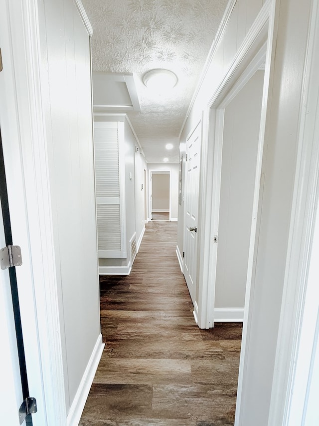 hallway featuring dark wood finished floors, visible vents, baseboards, and a textured ceiling