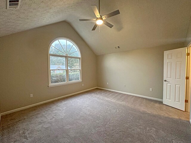 carpeted empty room featuring vaulted ceiling, ceiling fan, and a textured ceiling