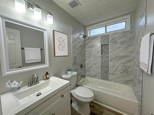 full bathroom with hardwood / wood-style floors, vanity, tiled shower / bath, toilet, and a textured ceiling