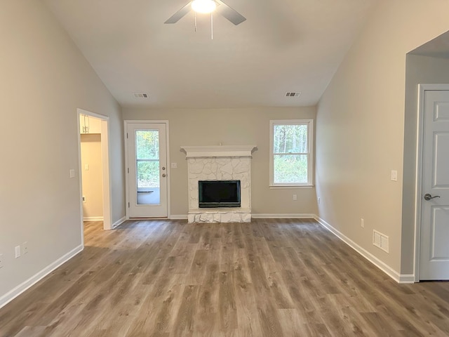 unfurnished living room featuring a healthy amount of sunlight, a stone fireplace, light hardwood / wood-style floors, and vaulted ceiling