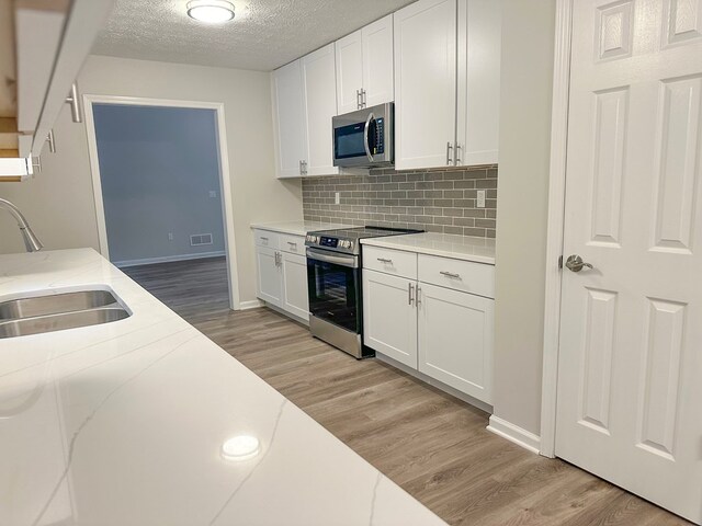 kitchen with a textured ceiling, sink, white cabinetry, and stainless steel appliances