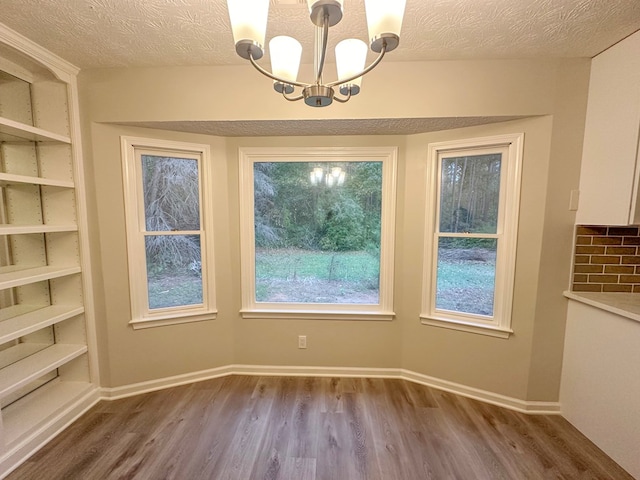 unfurnished dining area with hardwood / wood-style floors, a notable chandelier, and a textured ceiling