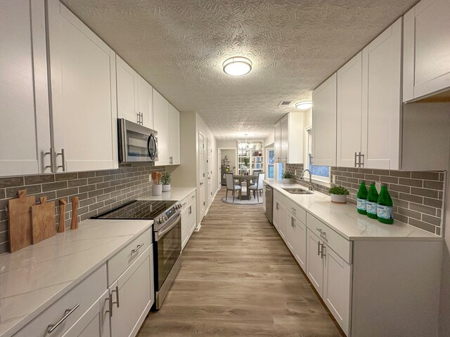 kitchen with sink, white cabinets, light wood-type flooring, and appliances with stainless steel finishes