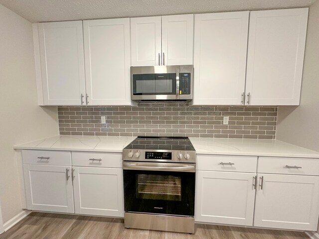 kitchen featuring backsplash, white cabinets, light stone countertops, light wood-type flooring, and stainless steel appliances