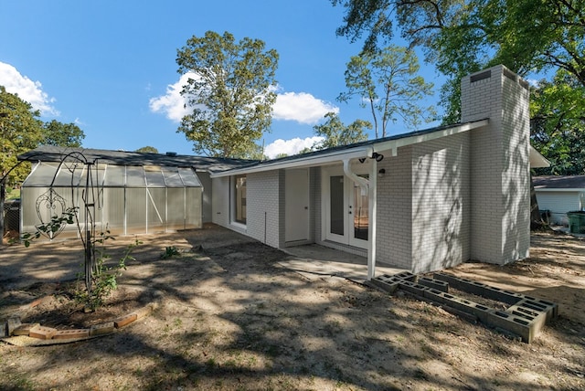 back of house with brick siding, an exterior structure, french doors, a chimney, and an outdoor structure