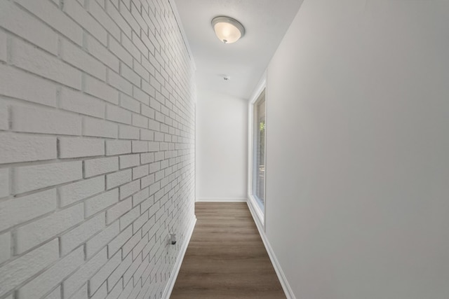 hall featuring an accent wall, baseboards, dark wood-style flooring, and brick wall