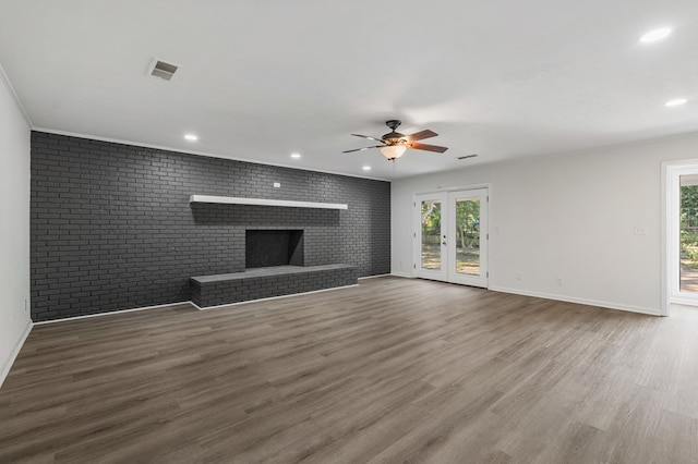 unfurnished living room featuring visible vents, brick wall, a fireplace, and wood finished floors