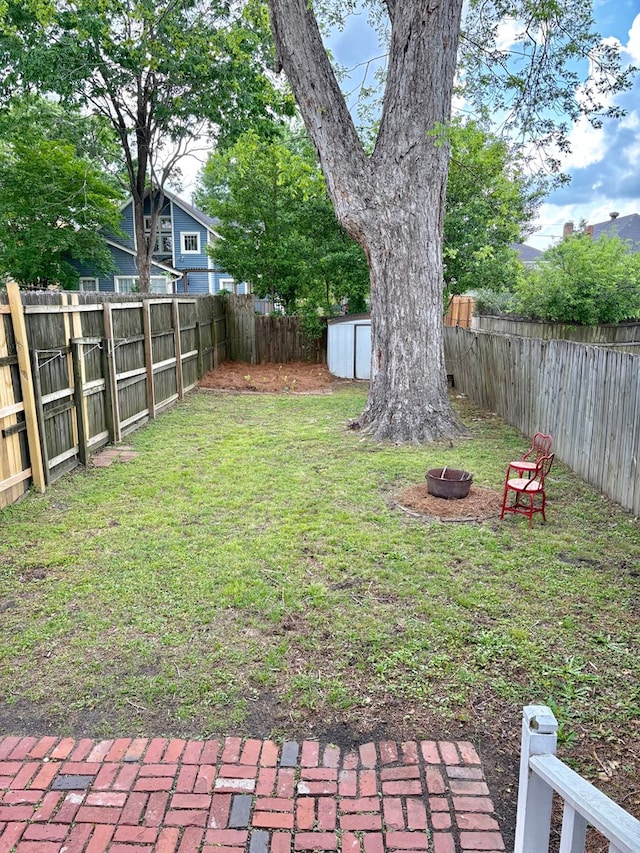 view of yard with a storage unit, an outdoor fire pit, an outbuilding, and a fenced backyard