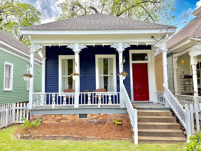 doorway to property featuring roof with shingles, covered porch, and fence