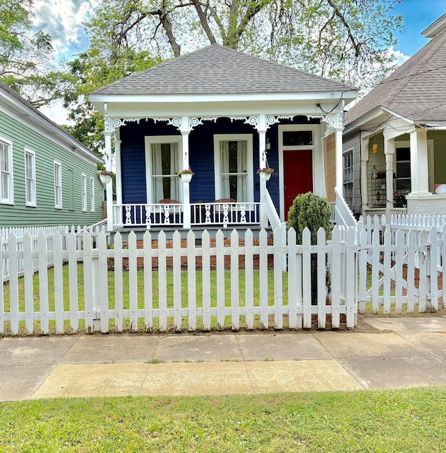 view of front facade featuring covered porch, a front lawn, a fenced front yard, and roof with shingles