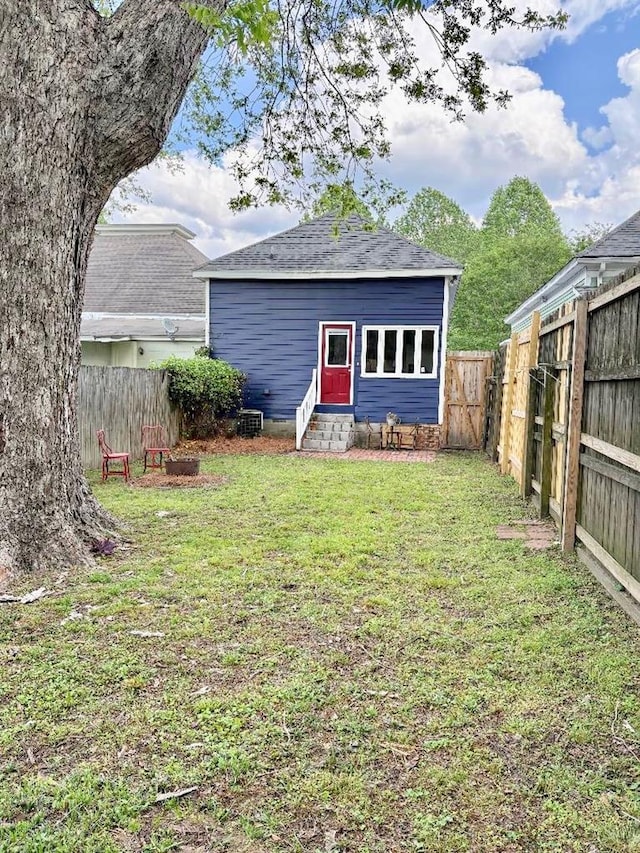 back of house featuring a lawn, roof with shingles, entry steps, and a fenced backyard