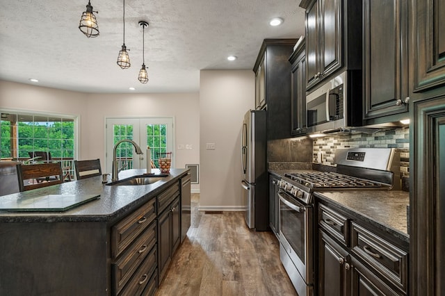 kitchen with a textured ceiling, appliances with stainless steel finishes, tasteful backsplash, a sink, and dark wood-type flooring