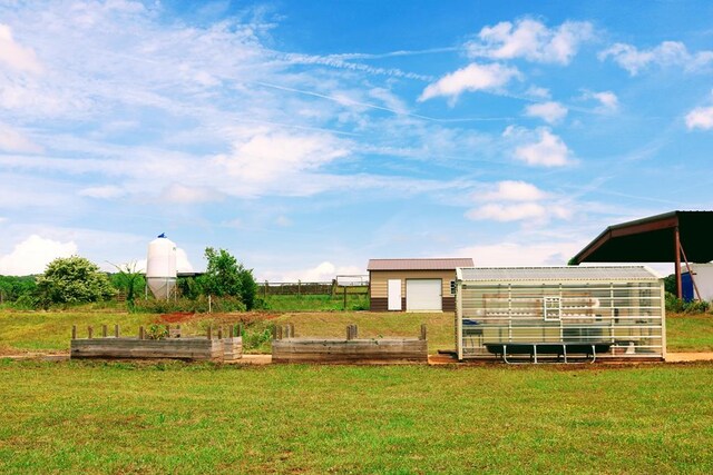 view of yard with fence, a detached garage, an outdoor structure, and a vegetable garden