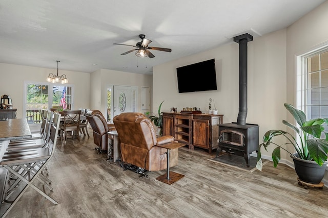 living room with a wood stove, light wood finished floors, and ceiling fan with notable chandelier