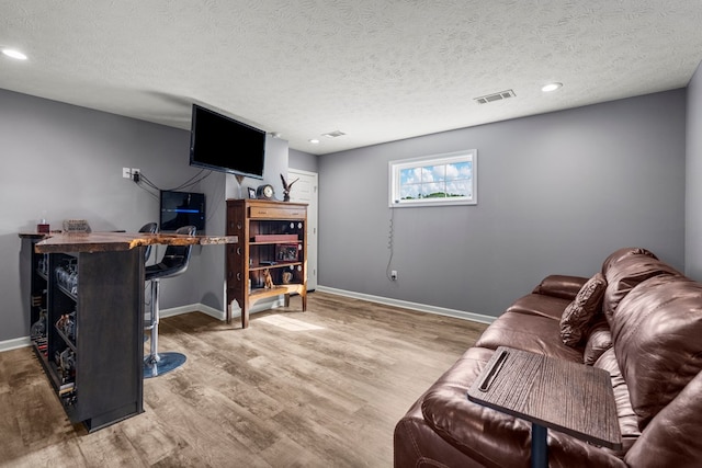 living room with baseboards, a textured ceiling, visible vents, and wood finished floors