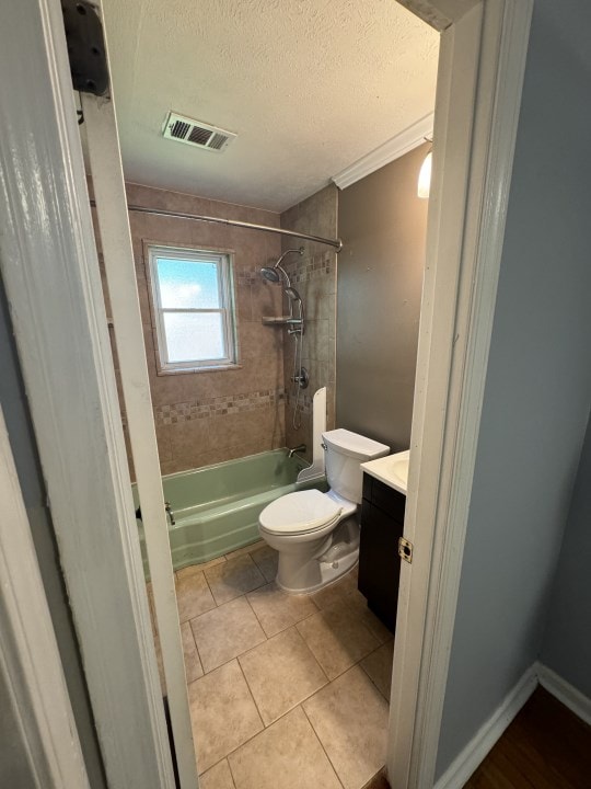 full bathroom with tiled shower / bath combo, tile patterned floors, a textured ceiling, toilet, and vanity