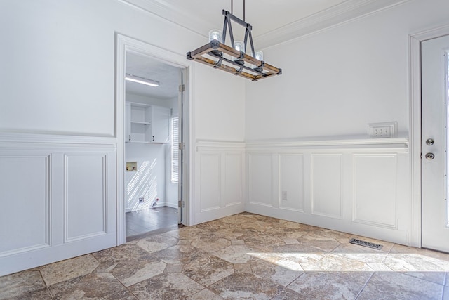 unfurnished dining area featuring wainscoting, stone finish flooring, crown molding, a decorative wall, and a notable chandelier