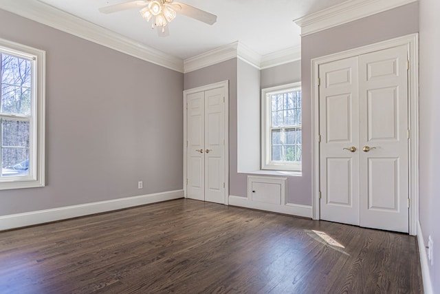 unfurnished bedroom featuring baseboards, a ceiling fan, ornamental molding, dark wood-type flooring, and multiple closets