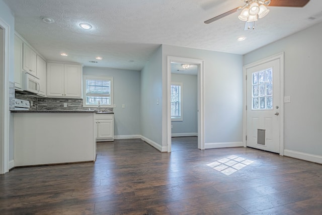 kitchen featuring white microwave, backsplash, white cabinets, and dark wood finished floors