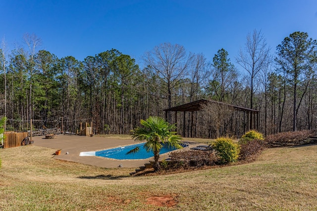 view of swimming pool featuring a patio, a wooded view, and a yard