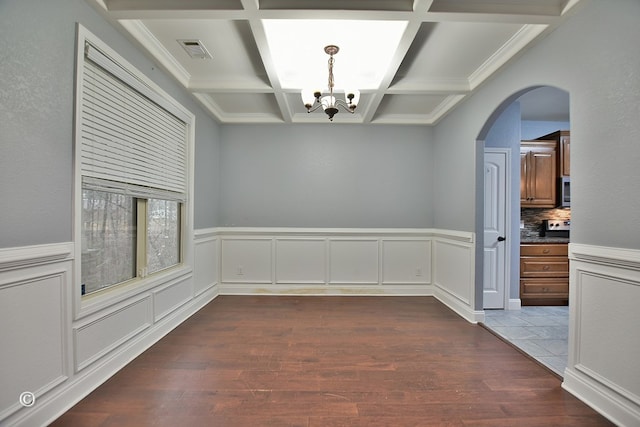 unfurnished dining area featuring a notable chandelier, beam ceiling, dark hardwood / wood-style flooring, and coffered ceiling