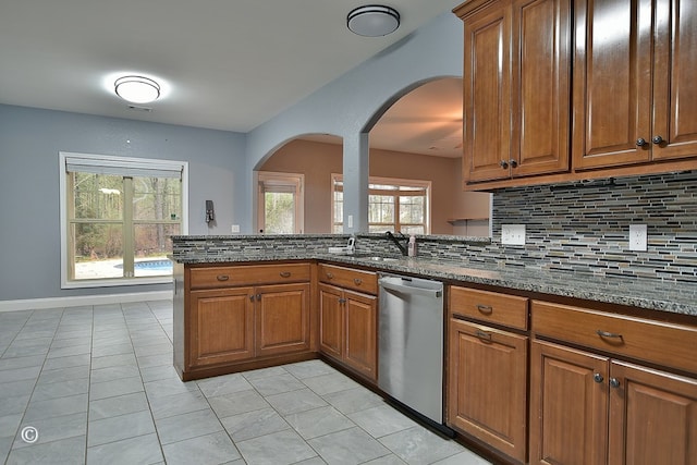 kitchen featuring dishwasher, a healthy amount of sunlight, dark stone countertops, and tasteful backsplash